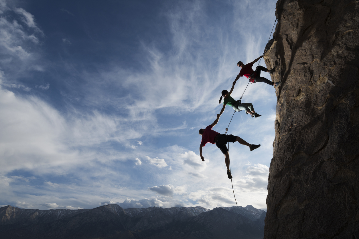 Trust. Three rock climbers helping one from falling.