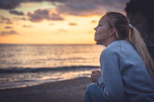 Thoughtful smiling woman looking with hope into horizon during sunset at beach